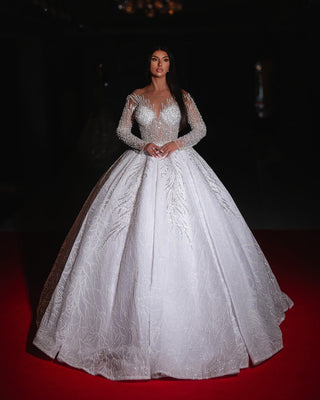 A luxurious beaded bridal ball gown with a shimmering full skirt, sheer neckline, and long embellished sleeves.