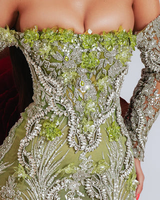 Close-up of the embellished off shoulder dress showcasing silver stones and green crystals.