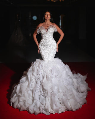 A glamorous mermaid-style wedding gown with intricate embroidery, an off-the-shoulder neckline, and a dramatic ruffled skirt.