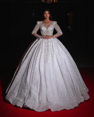 
Bride wearing an elegant white ball gown with long sheer sleeves and intricate embroidery.