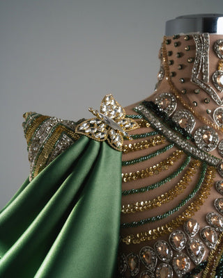 Luxury gown in beige and green satin, embellished with intricate crystals and sequins, featuring a sculptural design.