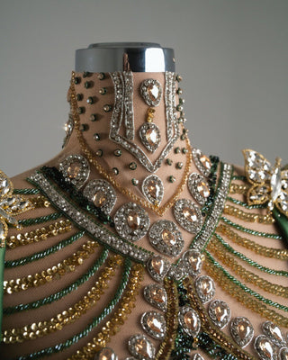 Dramatic green and gold dress adorned with sequins and gemstones, showcasing structured shoulders and hips.