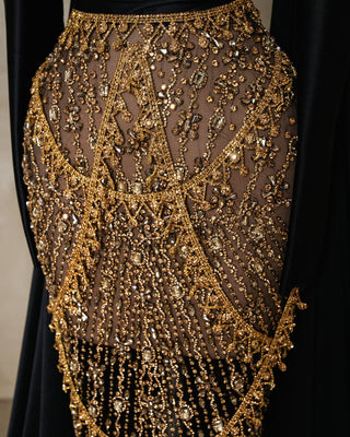 Close-up of black dress showing intricate gold stones and satin flower accents on the shoulder