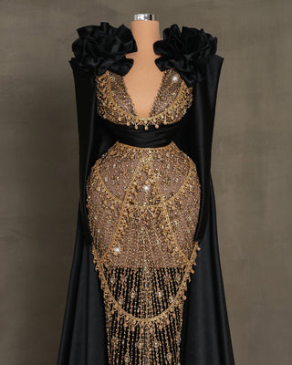 Black dress with gold stone embellishments, long satin sleeves, and flowing side capes