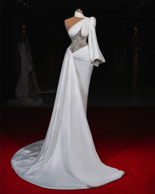 Modern white wedding dress featuring asymmetric draping and shimmering crystal details.