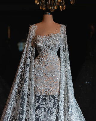 Elegant bridal gown with intricate lace and flowing cape sleeves.